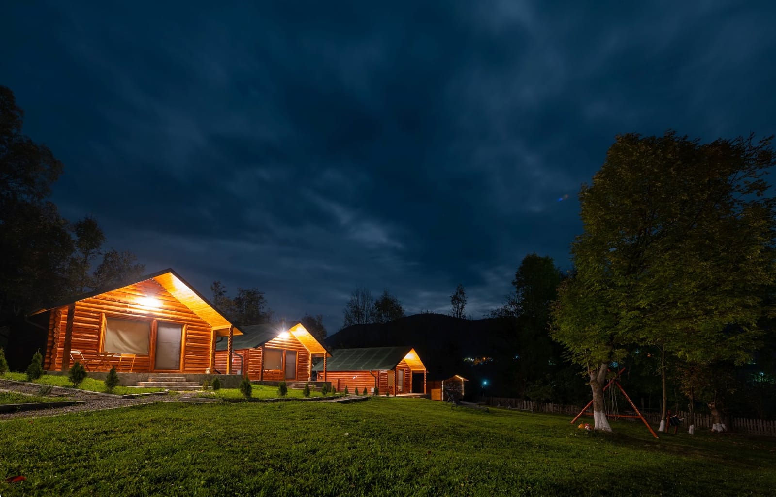 Cabanele iluminate, văzute din curte la lăsarea serii